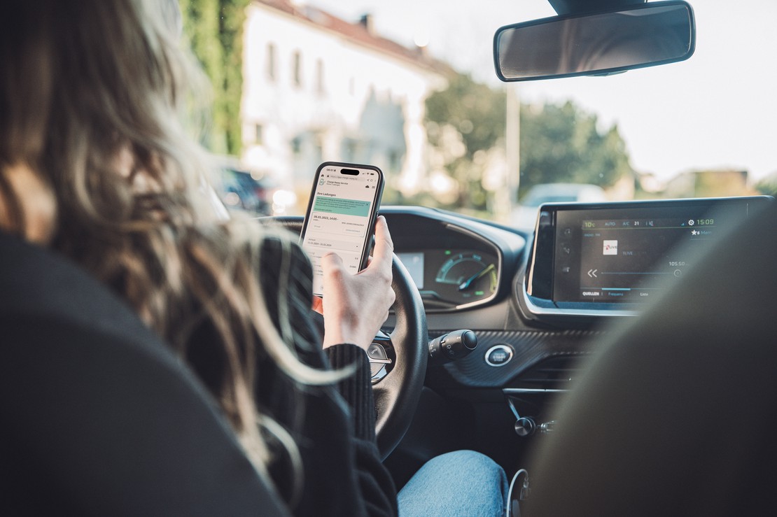 Frau im Auto mit Charge Repay Service auf dem Smartphone