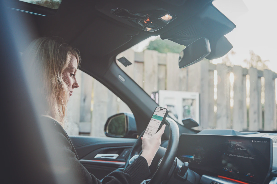 Frau nutzt den Charge Repay Service von Phoenix Contact auf dem Smartphone in einem parkendem Auto.