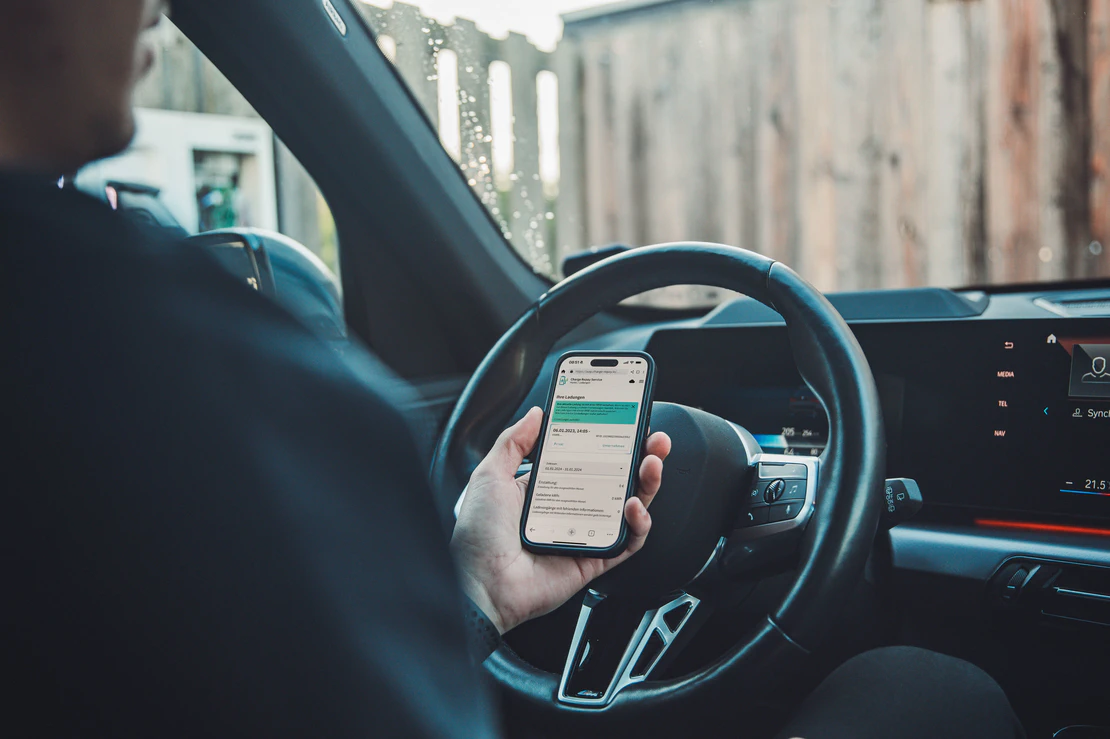 Ein man sitzt mit einem Smartphone im Auto. Auf dem Smartphone ist der Charge Repay Service geöffnet.